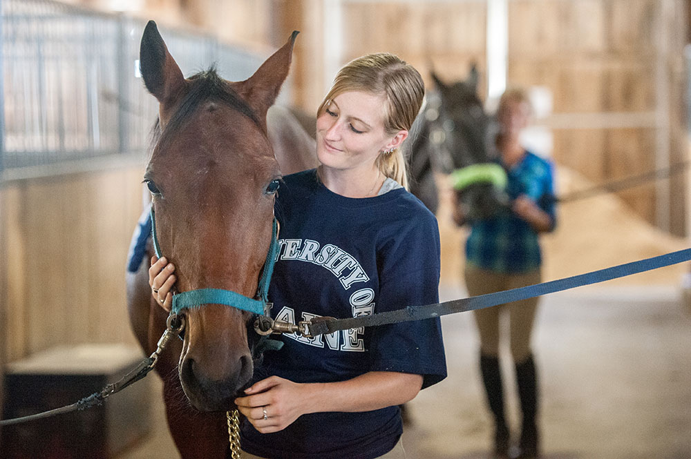 UMaine youth with her horse in a horse barn