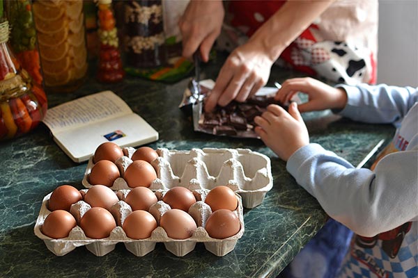 a parent and young child at a kitchen counter using eggs in a recipe