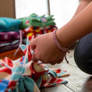 youth hands working on a fleece blanket project