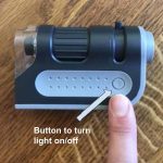 pocket microscope with persons finger indicating where button is located