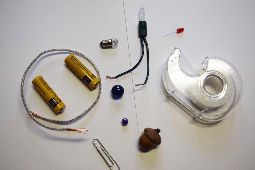 various elements of setting up a circuit: batteries, wire, small light bulbs, roll of tape, marbles and an acorn