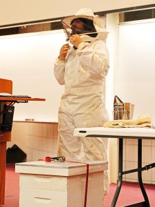 teenager giving a talk on beekeeping, wearing a beekeeping outfit and hat, 4-H Public Speaking event 2022