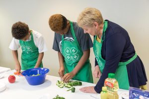 4-H volunteer assisting two 4-H youth members chopping vegetables