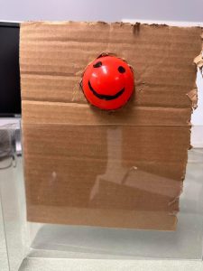 Plastic ball with a smiley face in a piece of cardboard