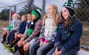 a group of elementary school aged 4-H members sitting on a bench in a school yard, all dressed in winter garments