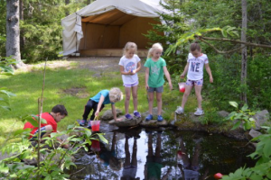 five children playing near a pond near a camp setting