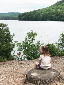 young girl sitting on a tree stump next to a lake