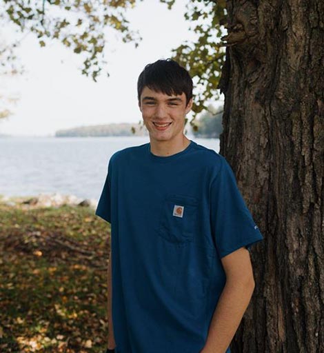 Cooper Dellarma standing by a tree by the water