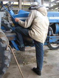 Man with cane climbs up on tractor