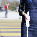 woman holding a white cane crossing a street