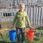 woman carrying 5 gallon bucket in each hand in a farm pasture