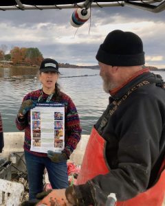 woman holding a poster talking to a fisherman on a boat