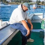 Man sitting on edge of lobser boat leaned forward stretching his back with his hands on his knees