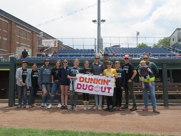 4-H members and leaders posing in the Portland Seadogs dugout, holding a banner reading "Dunkin' Dugout"