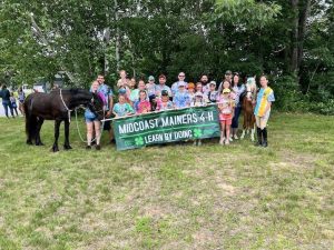 A large group of people and two horses holding a Midcoast Mainers banner