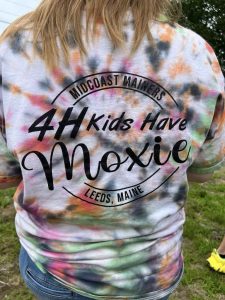 A person reading a t-shirt which says "4-H Kids Have Moxie"