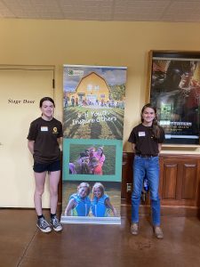 Two 4-H members standing in front of a poster, which reads "4-H Youth Inspires Others"