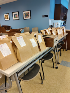 Rows of tables with brown paper bags, each containing onion orders.