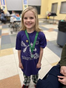 A smiling child wearing a 4-H pin and medal posing for a photo.