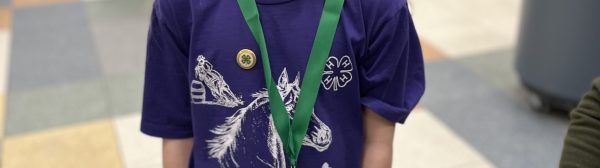 A smiling child wearing a 4-H pin and medal posing for a photo.