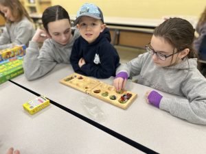 Three children sitting at a table, playing mancala.