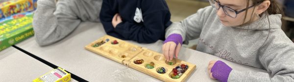 Three children sitting at a table, playing mancala.