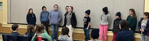 Several youths standing in a line at the front of a room. One appears to be speaking while others observe.