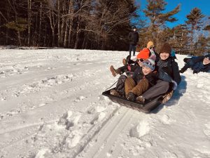 A group of kids smiling as they sled down a hill.