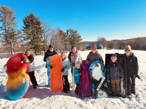 Eight youths posing with sleds on a snowy hill