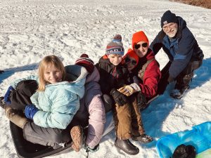 Jess Woodcock and kids sitting in a sled, with a man pushing them.