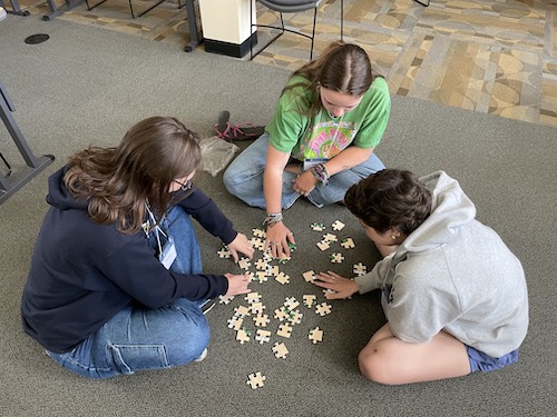 Intern Bailey doing a puzzle with two teens leaders.