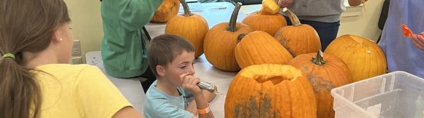 Children carving pumpkins at a table.