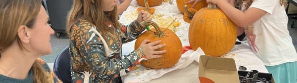 Children carving pumpkins at a table.