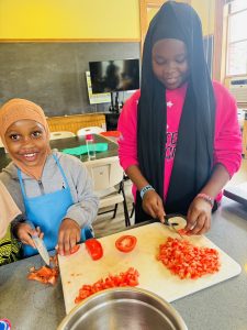 Two youths smiling while chopping tomatoes.