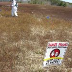 Spraying chemical material with a 4-nozzel boom sprayer with a pesticide warning sign in the fore-ground