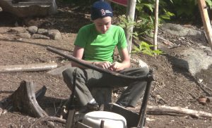 camper whittles chips from a branch to start a fire