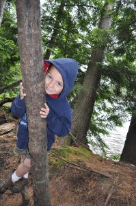 younf camper peeks around a tree