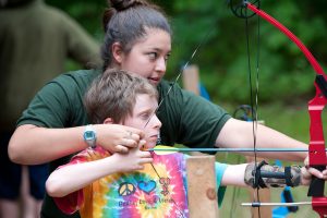 camp counselor helps camper learn to shoot a bow