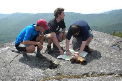 3 campers consult a map on a mountain top