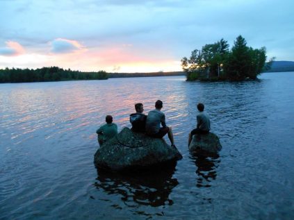 youth sitting on a rock in the lake at sunset