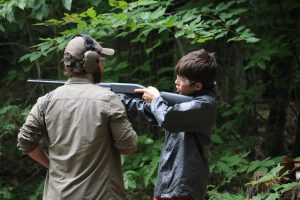 Male staff helping camper shoot a shotgun