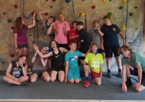 Two summer staff with a group of campers making goofy facing in front of the climbing wall