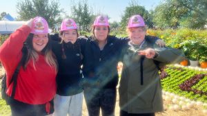 four participants in toy Jr. firefighters hats near a manicured garden