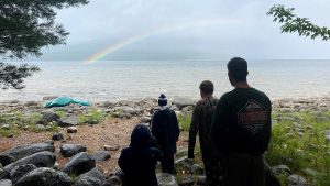 group of participants looking out towards a rainbow across a body of water