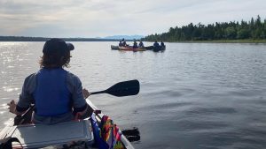 participant in a canoe facing a group of other participants in canoes on a lake