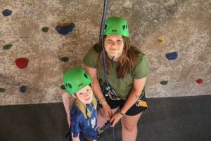 camper and camp counselor lookin up into camera. Counselor is tying camper in to climb the rock wall