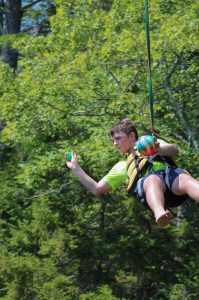 camper ziping down the zipline and throwing a ball during a survivor camp challenge