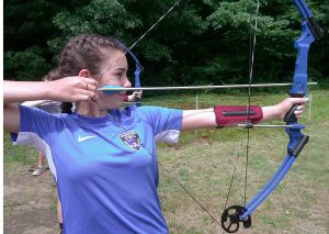Camper aims a compound bow and arrow during archery practice at Bryant Pond.