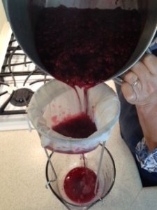 pouring cooked beach plums through cheesecloth into a container