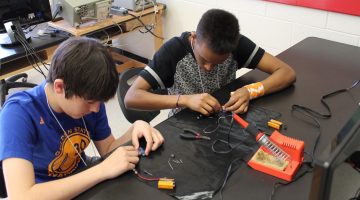 two teenagers building electronics at a table